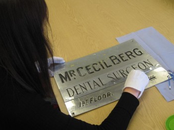 Curator working on object - a steel plate marked Mr Cecil Berg, Dental Surgeon